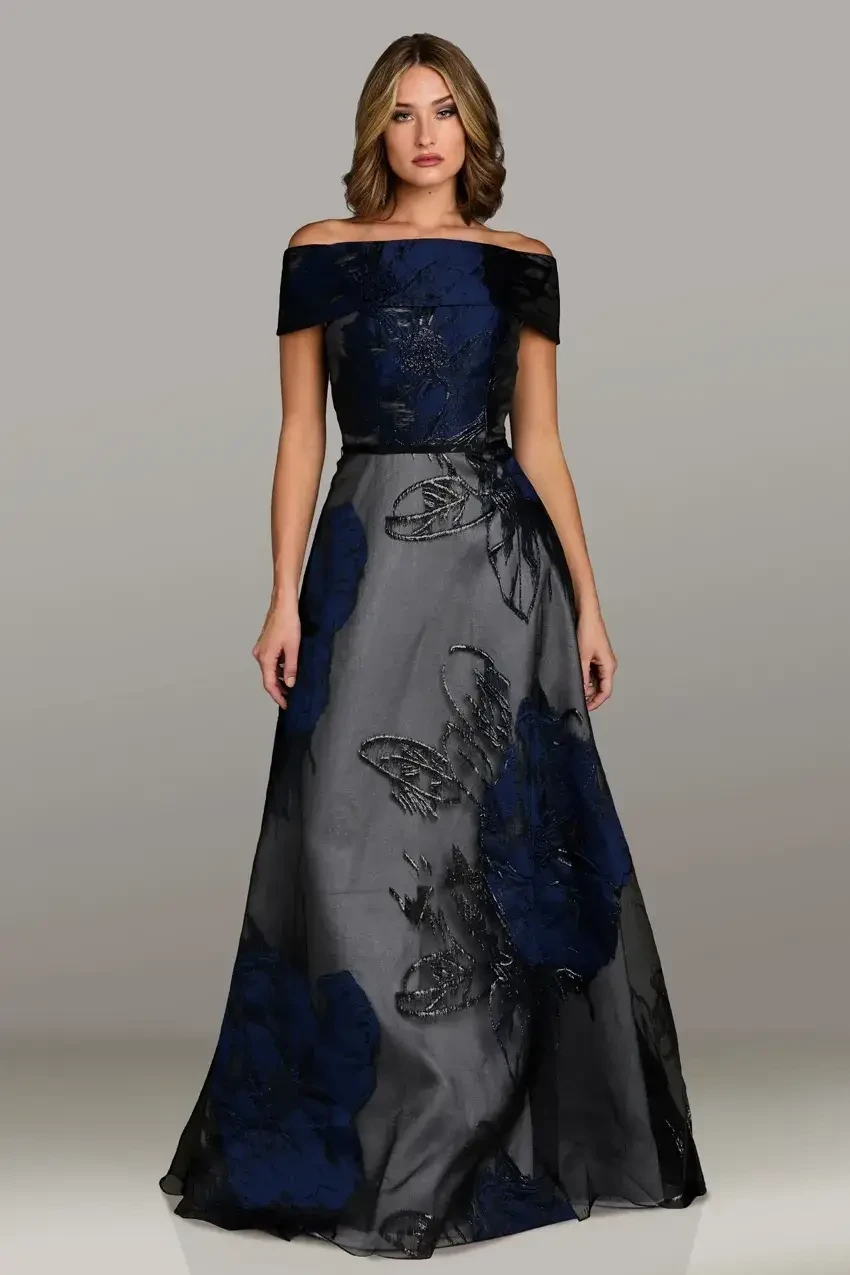 A woman wearing an elegant off-the-shoulder gown with a floral design in shades of navy and black.