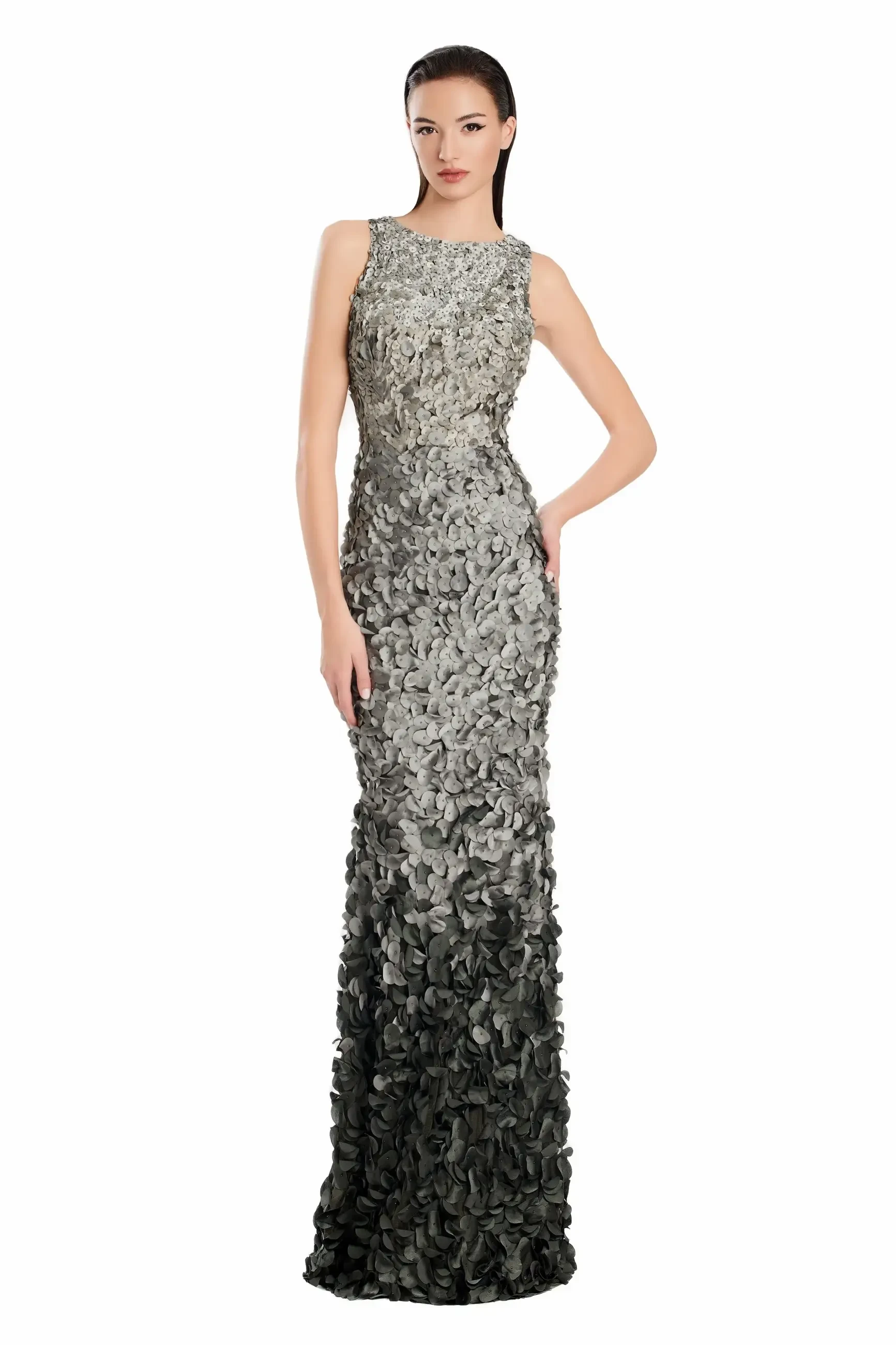 A model wearing a long, form-fitting gown adorned with layered textures resembling floral patterns in shades of grey.
