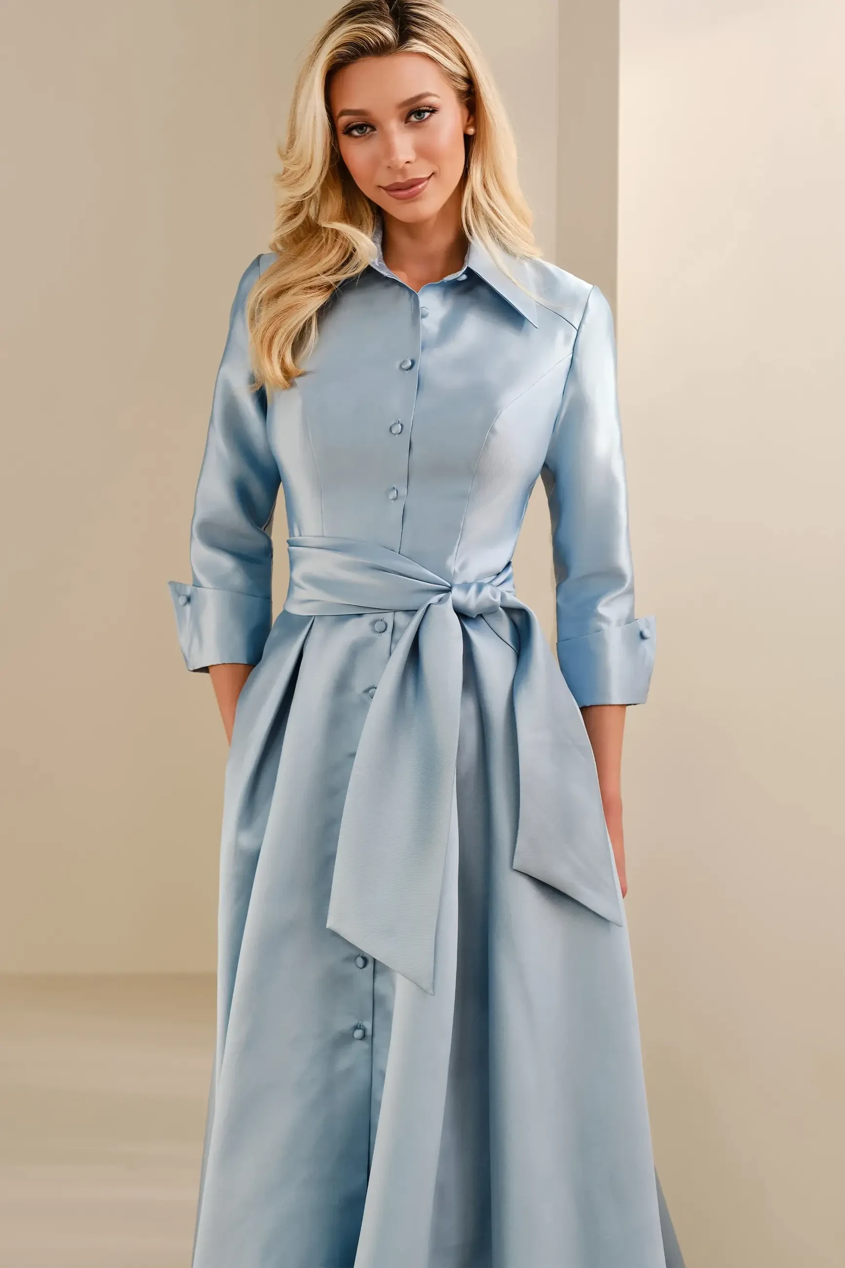 A woman in a light blue satin dress with a button-up front and a tied waist, standing against a neutral background.
